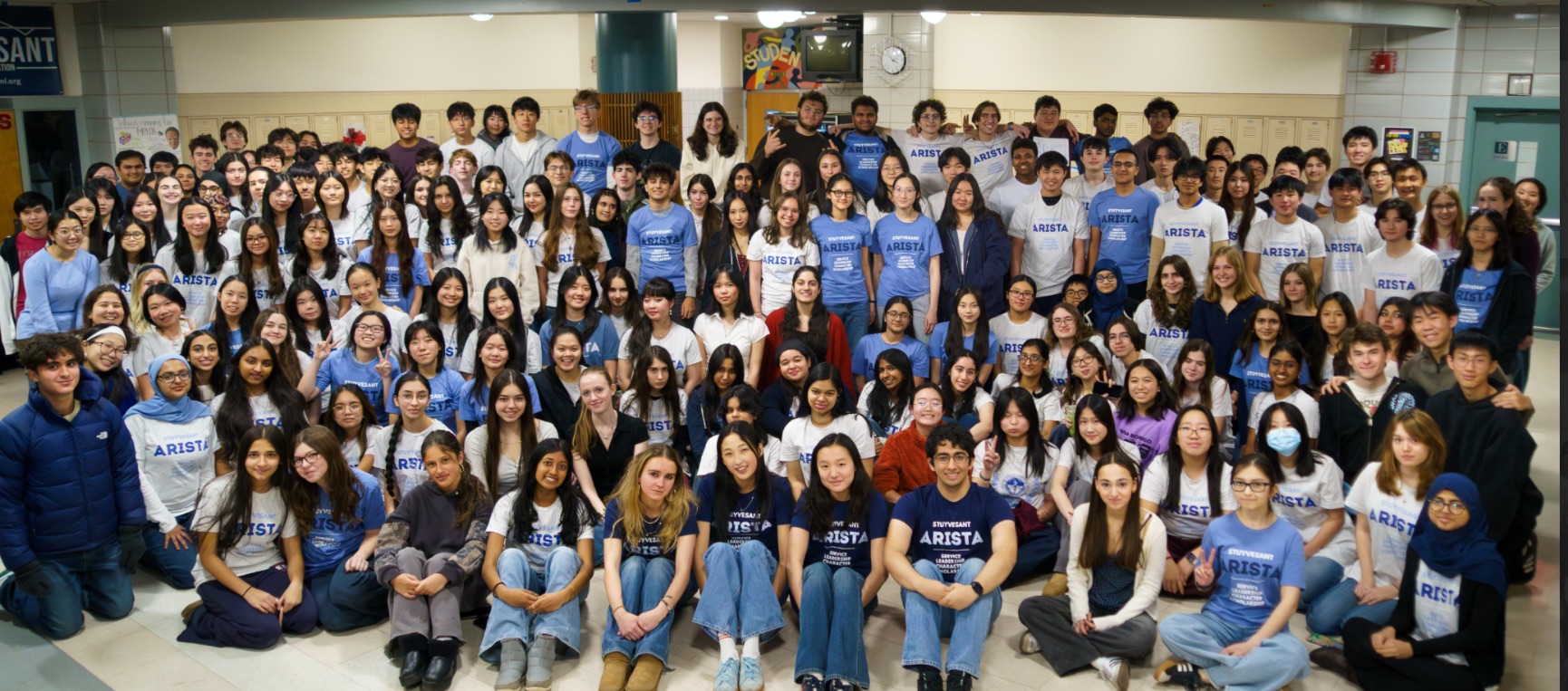 A large group of ARISTA members in ARISTA t-shirts, gathered together in a Stuyvesant hallway.